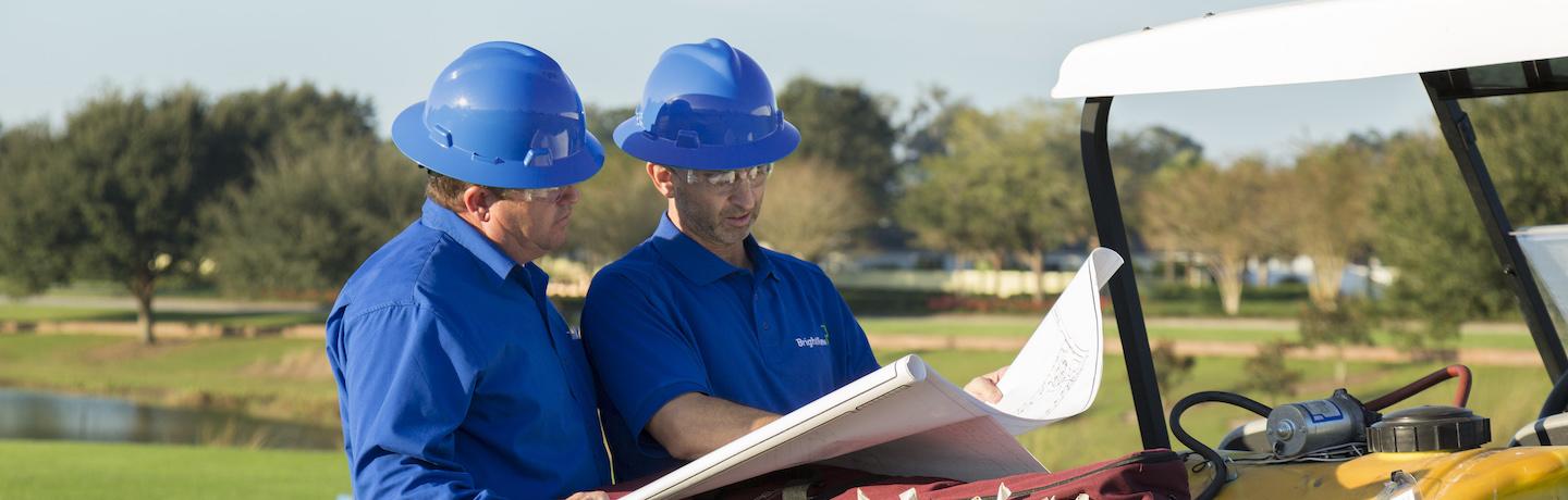 two golf course maintenance crew members discussing a blueprint