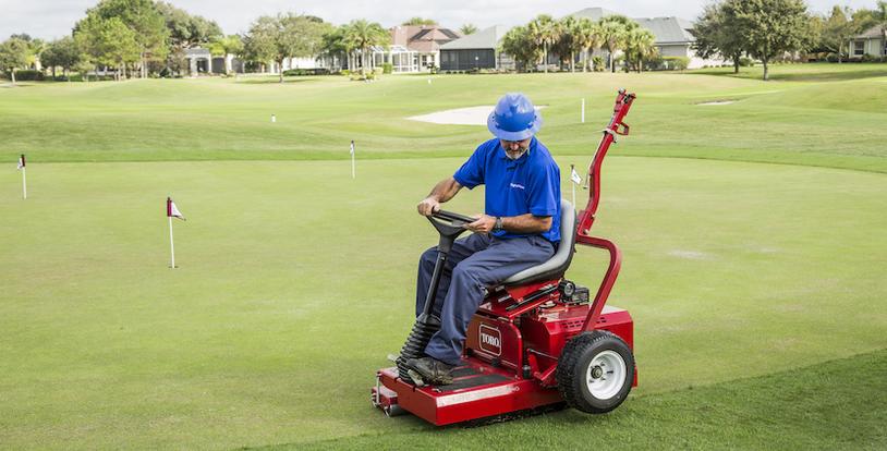 golf course maintenance crew member operating a roller